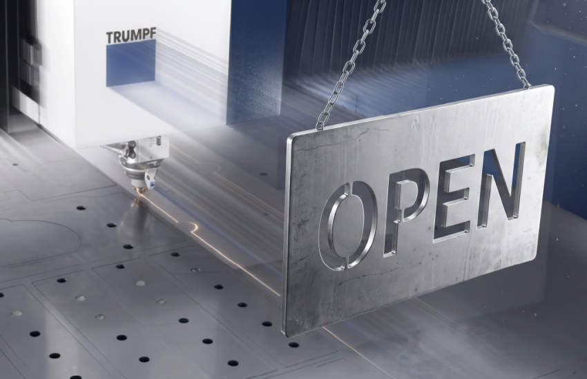 Pravokotna kovinska tablica z lasersko izrezanim napisom "OPEN", ki visi na kovinski verigi pred delujočim fiber laserjem Trumpf 12kW med razrezom pločevine.